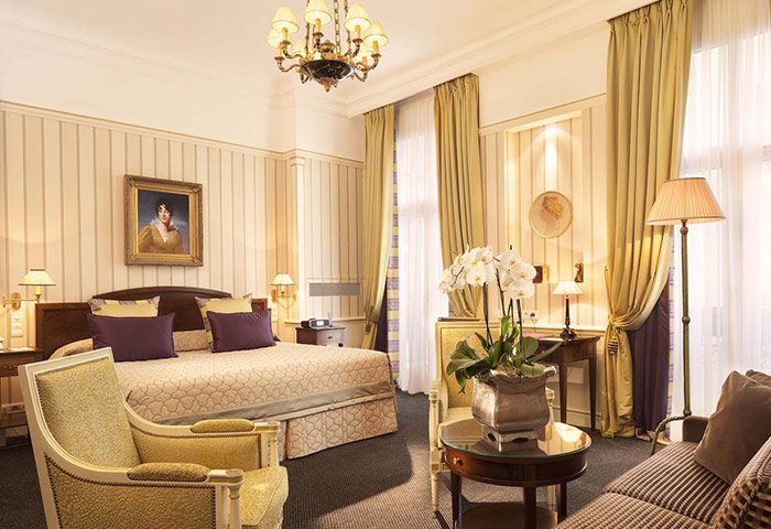 Hotel Napoleon luxury suite for gay couples' honeymoon. Elegant room with king bed, chandelier, and sitting area. Perfect for romantic travel.