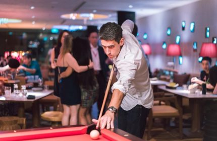 M Social Singapore: Man plays pool in stylish bar. Gay-friendly hotel offers nightlife and social scene for travelers.
