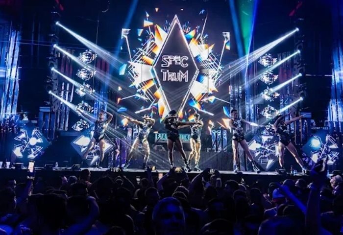 Madrid Gay Club: Dancers on stage at MACHO party. Crowd cheers, lights flash, and Spectrum logo shines. Gay nightlife travel.