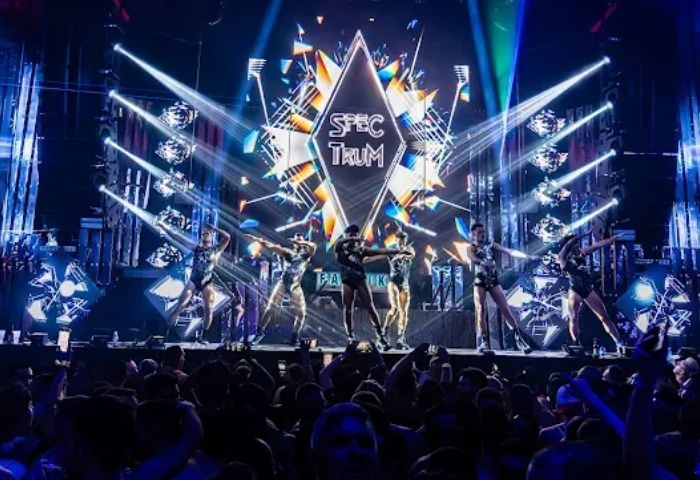 Madrid Gay Club: Dancers on stage at MACHO party. Crowd cheers, lights flash, and Spectrum logo shines. Gay nightlife travel.