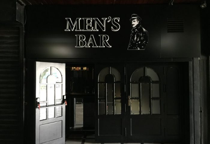 Men's Bar entrance in Torremolinos, Spain. Gay cruise club with dark facade and leather man silhouette. Gay travel guide.