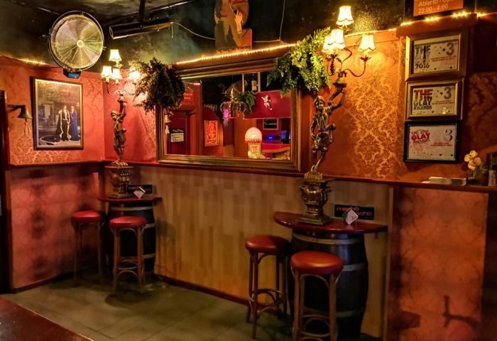 Interior of Macho Macho gay bar in Gran Canaria. Cozy atmosphere with barrel tables, red stools, and ornate decor. Gay travel destination.