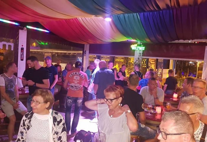 Patrons at Macho Macho Gay Bar in Gran Canaria. A lively gay bar scene with men enjoying drinks under colorful lights. Gay travel in Gran Canaria.