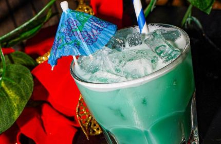 Macri Park gay bar cocktail. New York nightlife drink with ice, blue umbrella, and straw. Gay travel guide.