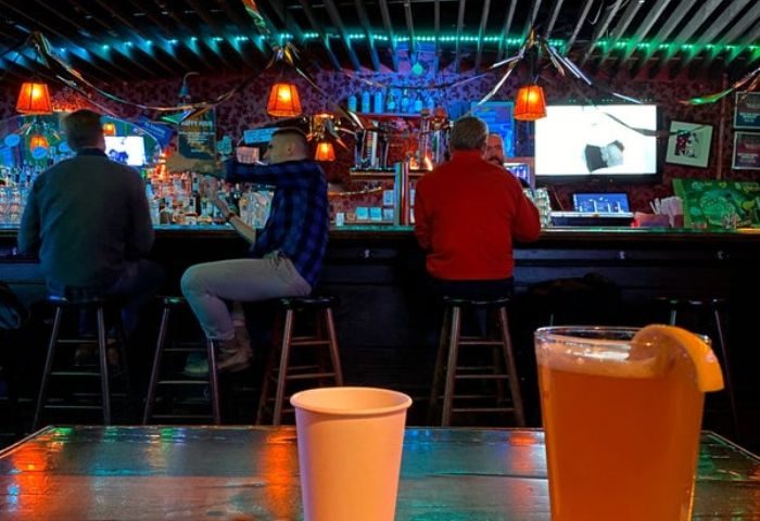 Macri Park gay video bar in New York. Interior shot of patrons at a bar with drinks. A glass of beer with a lemon wedge is in the foreground.
