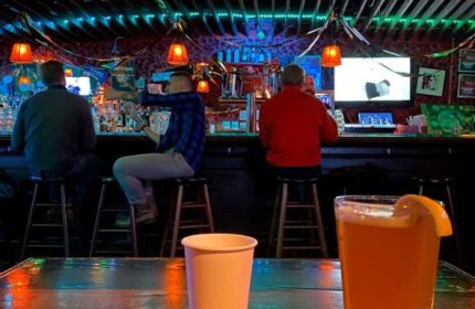 Macri Park gay video bar in New York. Interior shot of patrons at a bar with drinks. A glass of beer with a lemon wedge is in the foreground.