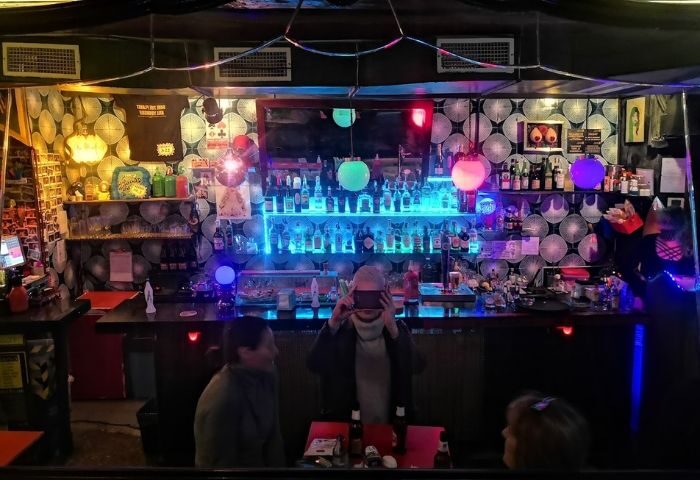 Madame Jasmine Gay Bar in Barcelona: Interior view of the bar with bottles, lights, and people. Gay travel destination.