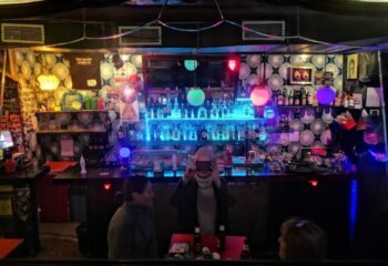 Madame Jasmine Gay Bar in Barcelona: Interior view of the bar with bottles, lights, and people. Gay travel destination.