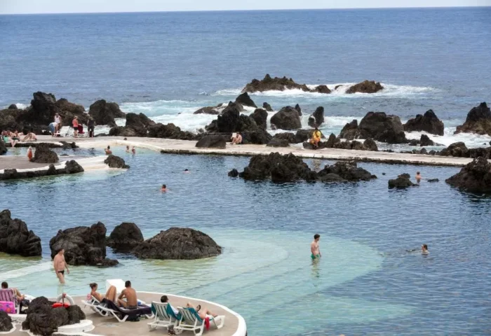Aqua Natura Madeira gay-friendly hotel pools. Oceanfront pools with people swimming and sunbathing. Volcanic rock formations add to the scenery.
