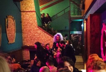 Interior of Malo Glitter Bar, Rome. Drag queen with purple hair, smiling people, and mirrors on the walls. Gay travel advice.