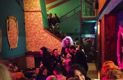 Interior of Malo Glitter Bar, Rome. Drag queen with purple hair, smiling people, and mirrors on the walls. Gay travel advice.