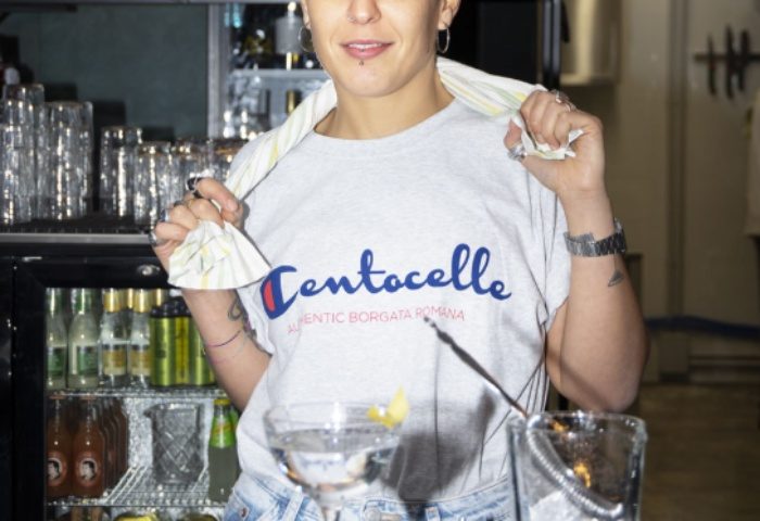 Malo Glitter Bar Rome: Bartender with Centocelle shirt, serving drinks. Gay travel advice for Rome's nightlife, bars, and gay-friendly spots.