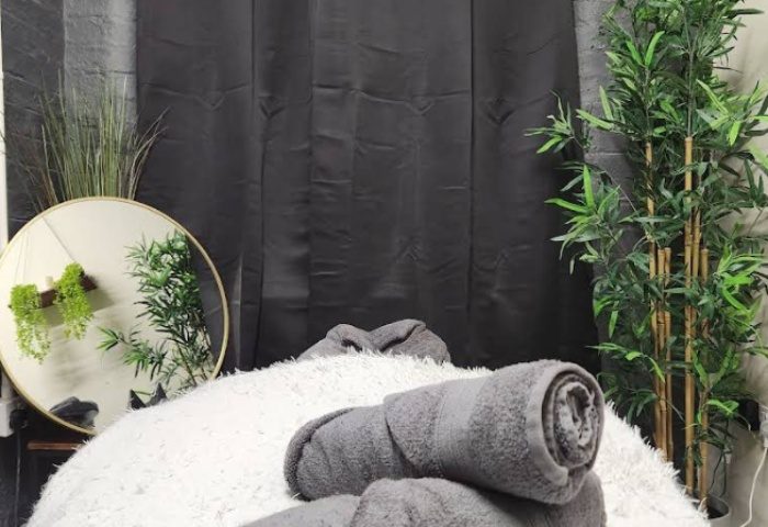 Manchester Queer Massage: Soft white massage table with rolled gray towels, plants, and a round mirror in a spa setting.