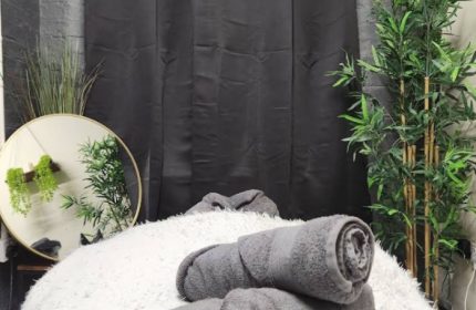Manchester Queer Massage: Soft white massage table with rolled gray towels, plants, and a round mirror in a spa setting.