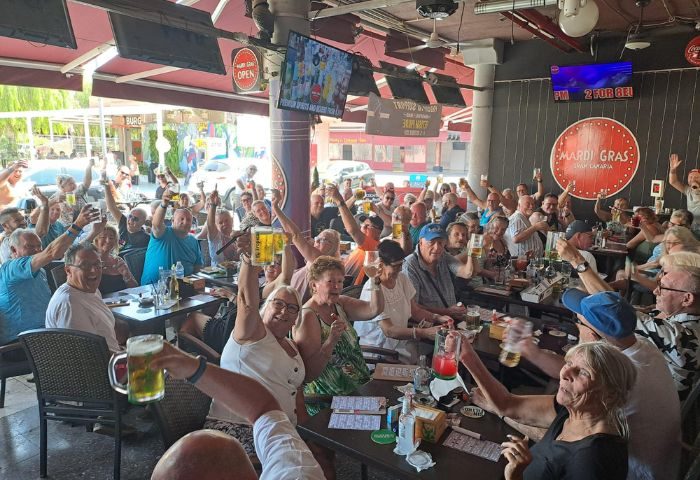 Mardi Gras Gay Bar in Gran Canaria: A lively crowd of gay men and women cheers with drinks at the popular gay bar, a top travel destination.