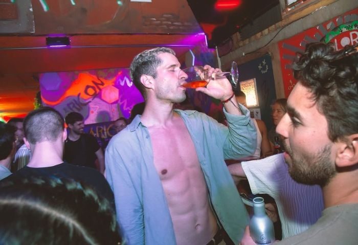 Gay bar in Barcelona: Man drinking at Maricon Ghetto-Friendly Bar. Nightlife scene with shirtless man and drinks. Gay travel in Spain.