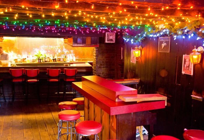 Marie's Crisis Sing-a-Long Bar in New York. Red stools line the bar, with colorful lights overhead. A popular gay bar in NYC.