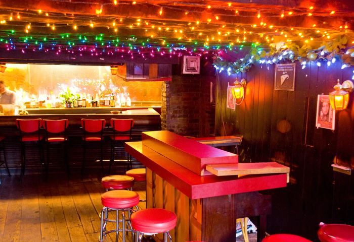 Marie's Crisis Sing-a-Long Bar in New York. Red stools line the bar, with colorful lights overhead. A popular gay bar in NYC.