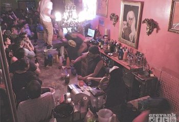 Marrakech Salon Gay Bar in Mexico: Lively scene in a gay bar. People drinking, bartender mixing drinks, and a person standing on the bar.