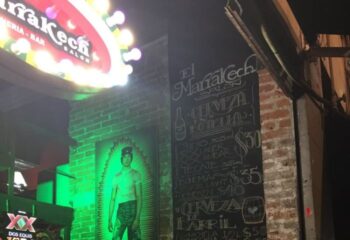 Marrakech Salon gay bar in Mexico. Menu board with beer prices, brick wall, and a neon sign. Gay travel destination.