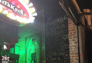 Marrakech Salon gay bar in Mexico. Menu board with beer prices, brick wall, and a neon sign. Gay travel destination.