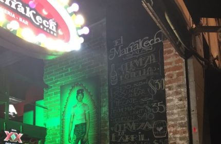 Marrakech Salon gay bar in Mexico. Menu board with beer prices, brick wall, and a neon sign. Gay travel destination.