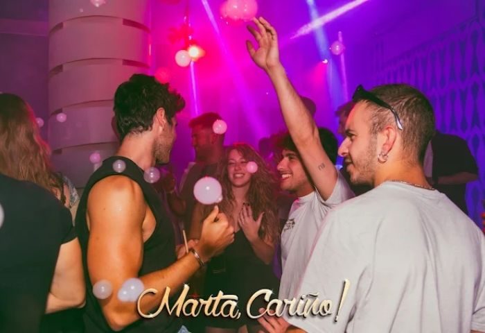 People at Marta Cariño gay club in Madrid. Nightlife scene with pink lights, bubbles, and happy gay men. Gay travel advice.