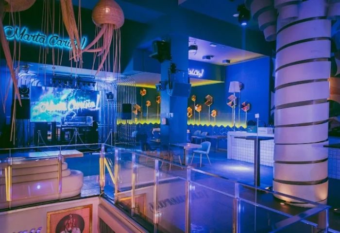 Interior of Marta Cariño, a gay club in Madrid. Blue lighting, stage, jellyfish lamps, and modern decor create a vibrant atmosphere.
