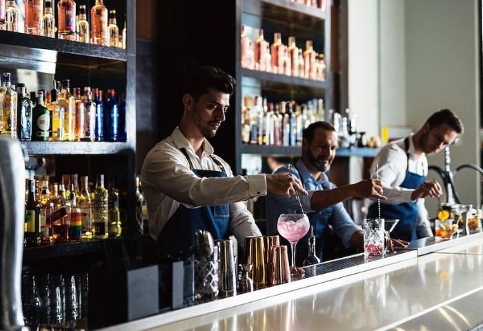 Bartenders craft cocktails at Marta Cariño, a gay club in Madrid. Shelves of liquor bottles line the bar. Madrid's nightlife.