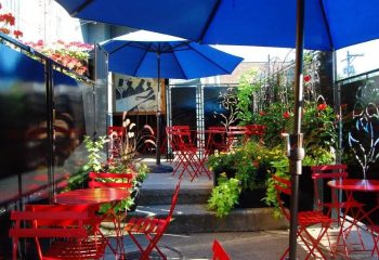 Outdoor patio at Marty's Martini Bar, a gay bar in Chicago. Red chairs and tables under blue umbrellas, plants, and decorative screens.