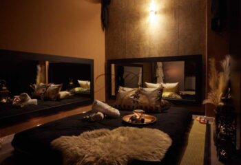 Gay massage in Barcelona: Luxurious massage room with bed, pillows, towels, and decorative items. Mirrors enhance the ambiance.