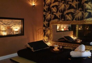 Gay massage in Barcelona: Luxurious massage room with black linens, gold accents, palm wallpaper, and candles for a relaxing experience.