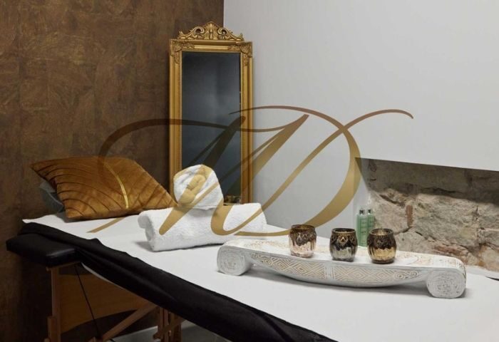Gay massage in Barcelona: Massage table with towels, pillow, golden mirror, and decorative elements in a luxurious spa setting.