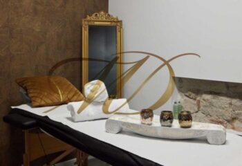 Gay massage in Barcelona: Massage table with towels, pillow, golden mirror, and decorative elements in a luxurious spa setting.