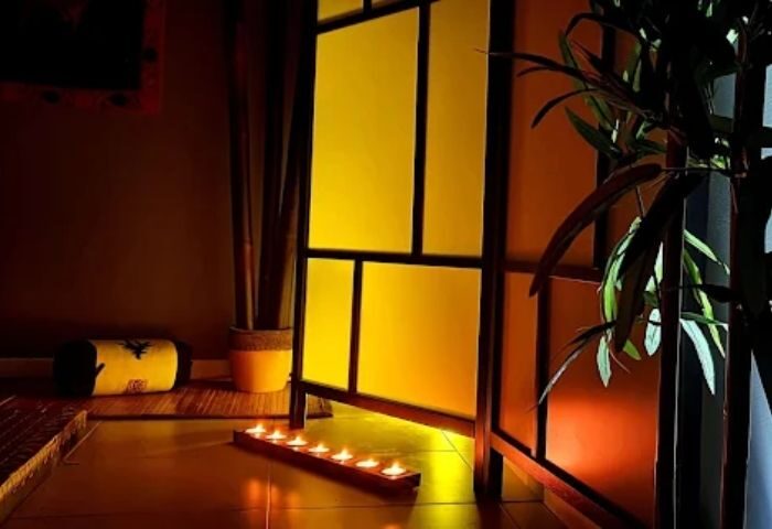 Madrid gay massage ambiance: Candles illuminate a serene space with a room divider, plants, and cushions, promising relaxation.