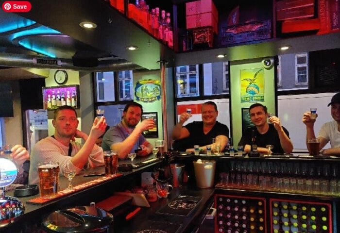 Gay travelers at Masken Bar in Copenhagen. Men toasting with shots, enjoying the nightlife. Gay bar scene, travel advice.