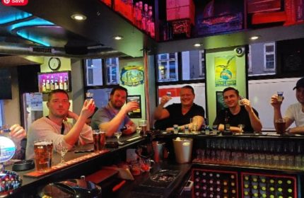 Gay travelers at Masken Bar in Copenhagen. Men toasting with shots, enjoying the nightlife. Gay bar scene, travel advice.