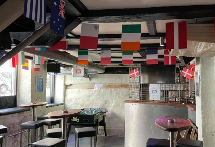 Masken Bar Copenhagen interior. Flags hang from the ceiling. Foosball table, bar stools, and tables. Gay travel advice.