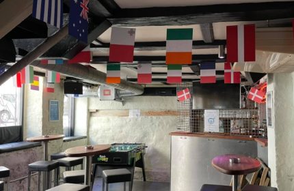Masken Bar Copenhagen interior. Flags hang from the ceiling. Foosball table, bar stools, and tables. Gay travel advice.