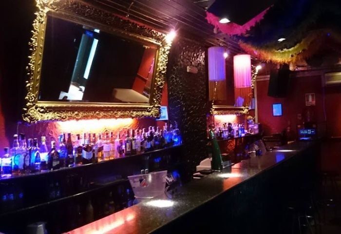 Medaigual Gay Bar in Madrid's Chueca. Bottles line the bar under a gold mirror. A popular spot for gay men's travel in Spain.