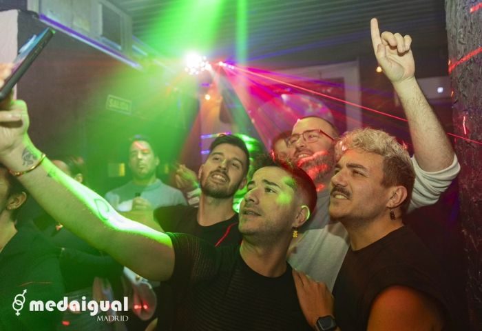 Gay men take a selfie at Medaigual gay bar in Chueca, Madrid. Nightlife scene with colorful lights. Gay travel advice in Madrid.
