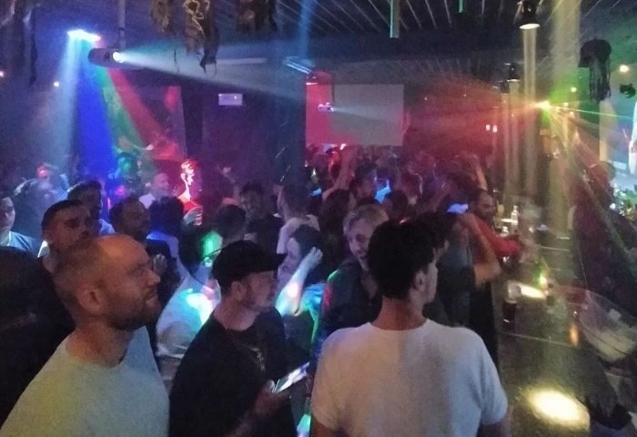Medaigual Gay Bar in Madrid's Chueca. Crowded dance floor with men under colorful lights. Gay nightlife and travel in Spain.