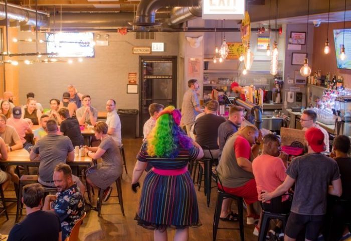 Interior of Meeting House Tavern, a unique gay bar in Chicago. People at tables and bar, rainbow wig and dress.