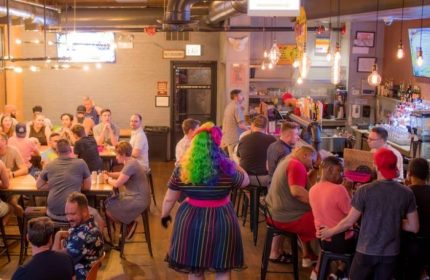 Interior of Meeting House Tavern, a unique gay bar in Chicago. People at tables and bar, rainbow wig and dress.
