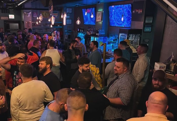 Crowded scene inside Meeting House Tavern, a unique gay bar in Chicago. Many men are socializing, drinking, and enjoying the atmosphere.