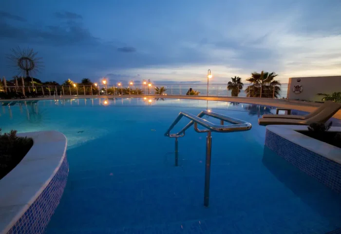 Meliá Madeira Mare Hotel pool at dusk. Gay travel in Funchal, Portugal. Relaxing vacation spot with ocean views. Palm trees and lounge chairs.