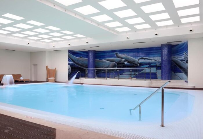 Indoor pool at Meliá Madeira Mare, a gay-friendly hotel. Whale mural, waterfall features, and lounge chairs create a relaxing atmosphere.