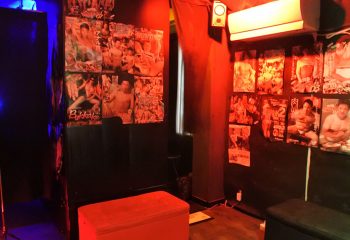 Interior of Men's Club MEAT Tokyo, a popular gay cruise club in Ni-Chome. Walls are covered in posters of muscular men. Red lighting.