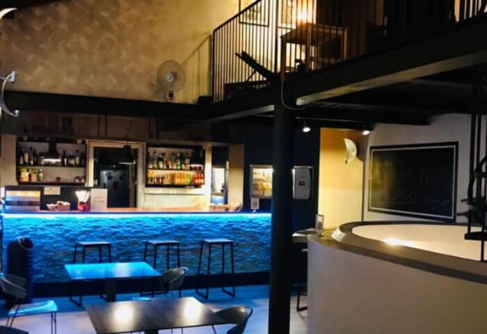 Metro Sauna Centrale Milan bar area. Blue lit bar with stools, tables, and a mezzanine level. Gay sauna travel advice.