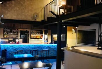 Metro Sauna Centrale Milan bar area. Blue lit bar with stools, tables, and a mezzanine level. Gay sauna travel advice.